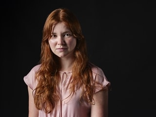 Law student Agata looks at the camera, the background is dark. Agata is wearing a pink top, Agata's hair is long and ginger.