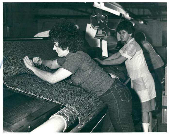 An old black and white photo of two women making finishing touches to a large carpet